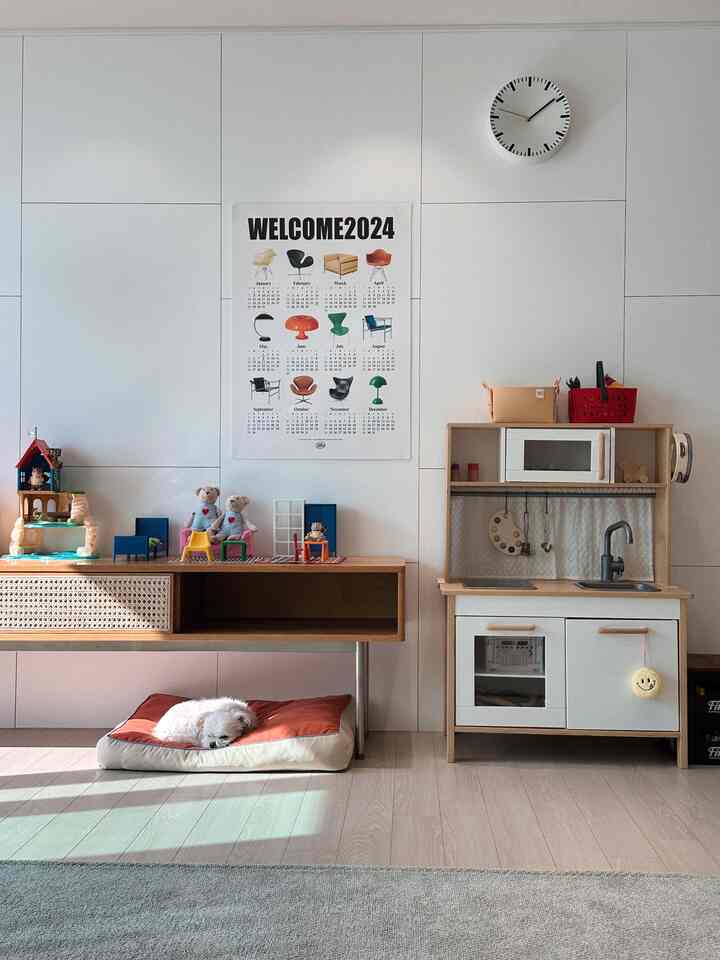 白い壁とナチュラルな木製家具が配置されたリビング、子供のおもちゃとペットベッドが調和した印象的な空間