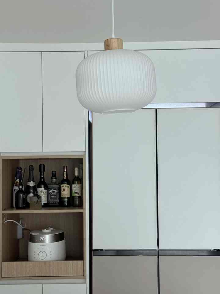 白を基調としたキッチン、冷蔵庫と炊飯器、ホームバー用の酒瓶が配置された清潔感のある空間