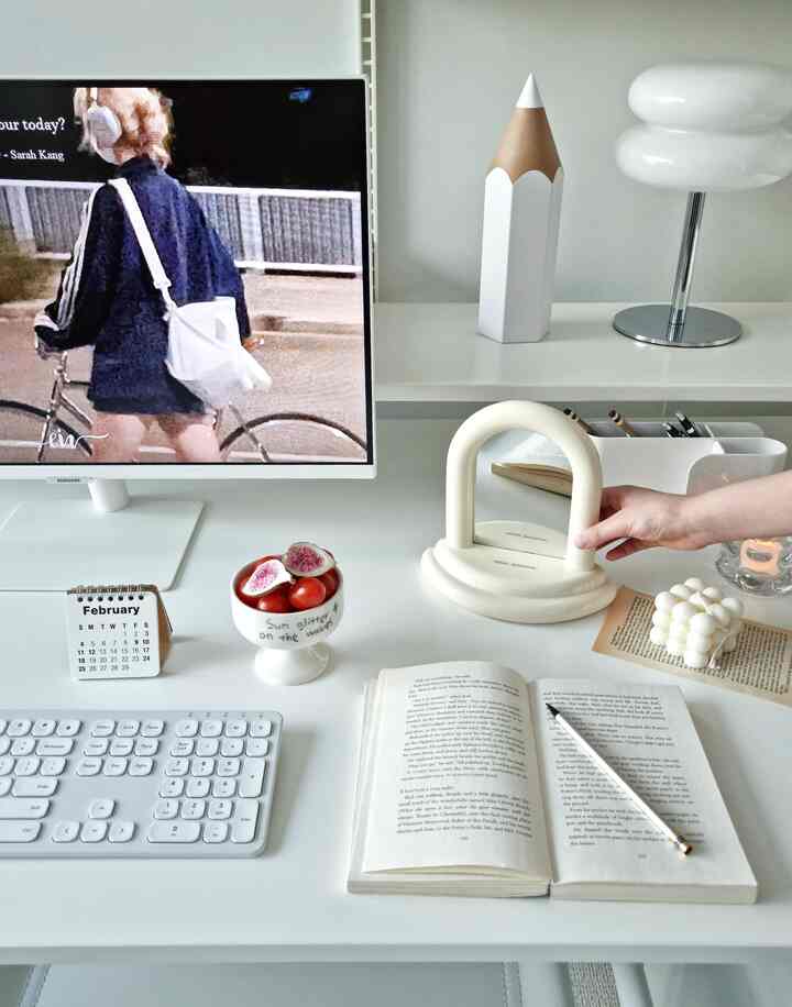 White-toned home office space featuring mid-century modern lamp and ceramic mirror on a clean desk interior