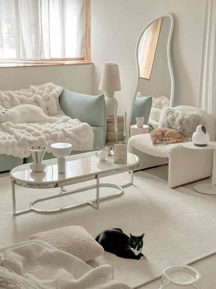 Natural color-toned living room with light blue sofa, two cats resting on armchair and carpet creating a minimal ambiance