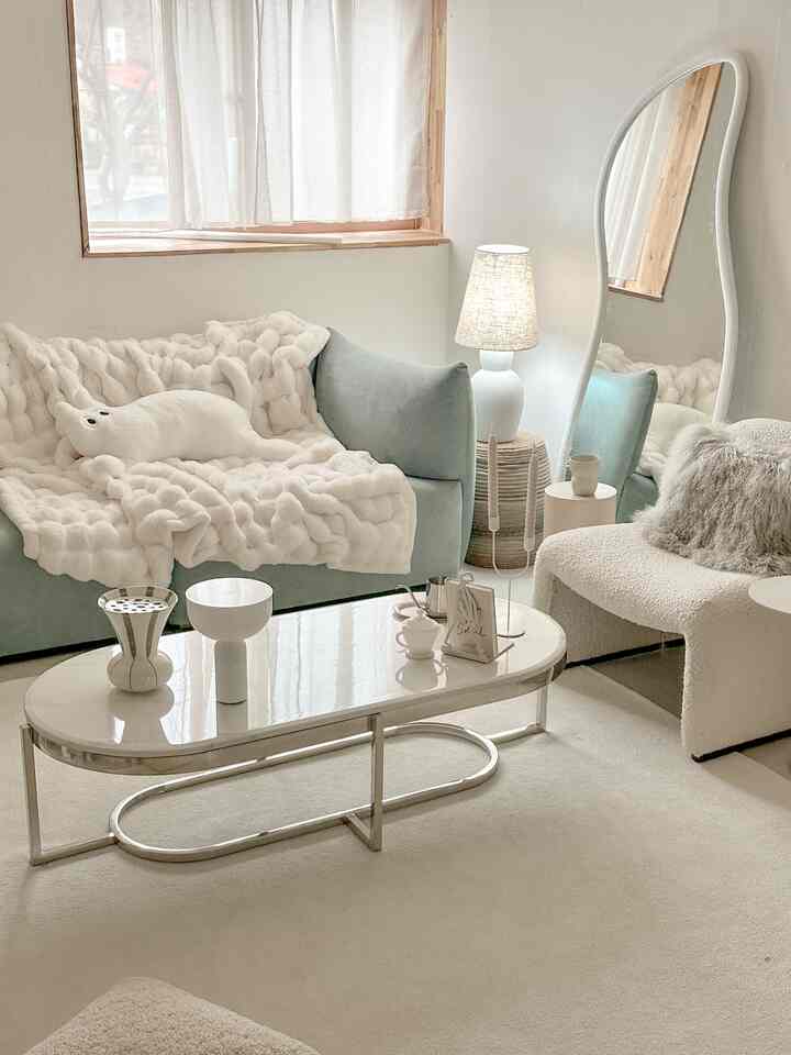 A cozy living room with soft natural and white tones featuring a sofa, armchair, standing mirror, and floor lamp in a simple design