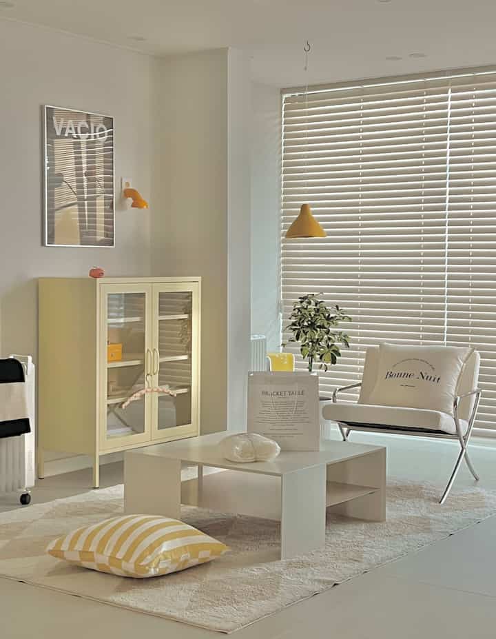 White and yellow toned living room featuring floor cushion seating, low table, and lounge chair with a clean and warm atmosphere