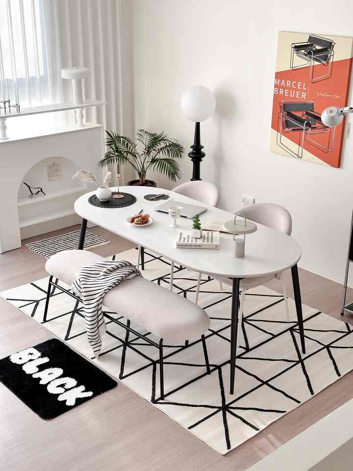 白と黒のトーンでまとめられたリビング、セラミックのダイニングテーブルとベンチ、幾何学的なカーペットが配置されたモダンなインテリア