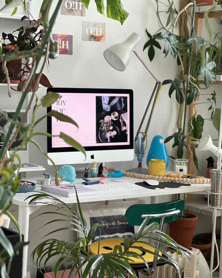 White and green toned home office featuring an Apple iMac on desk surrounded by plants in cozy workspace