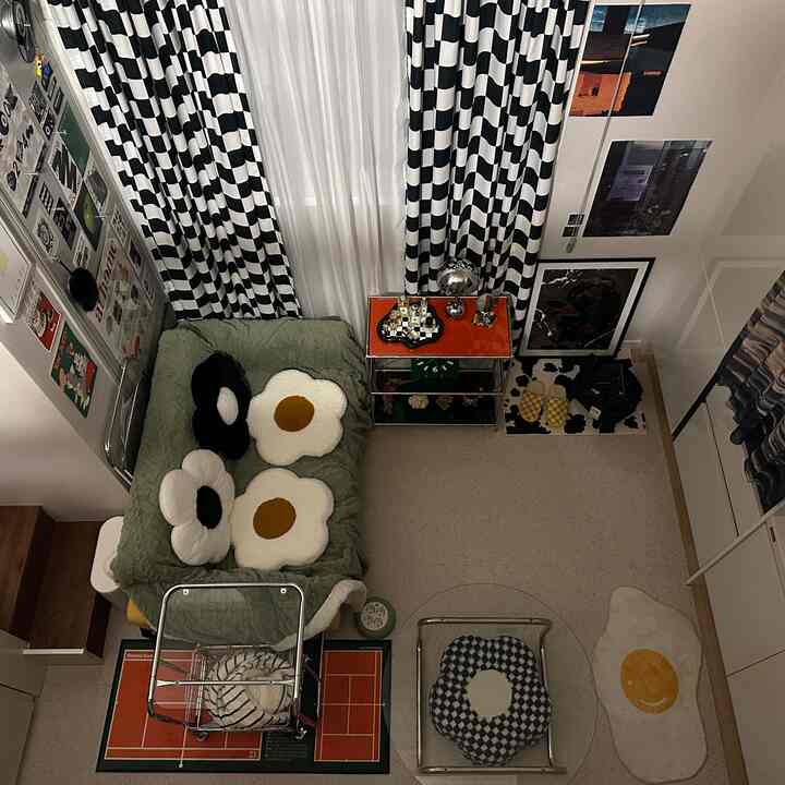 透明な家具とオレンジ色のサイドテーブルが配されたコンパクトなワンルーム、モノトーンのストライプカーテンと卵型のラグが印象的なモダンな空間