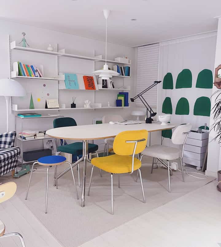 White and light gray toned dining room featuring colorful dining chairs in a mid-century modern setting