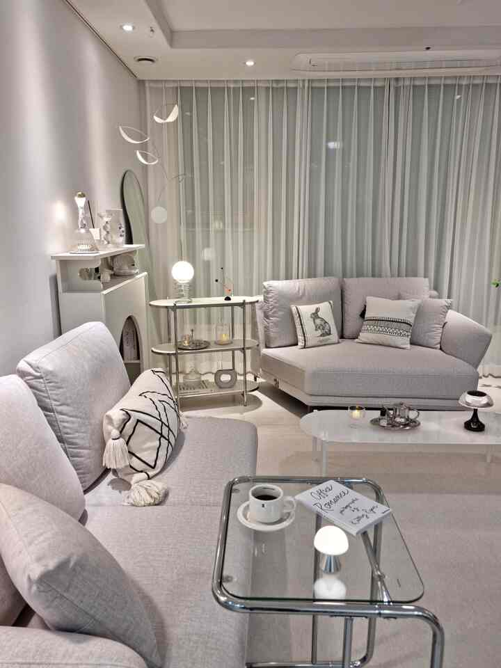 A white-toned living room featuring modular fabric sofas and transparent glass sofa tables, creating a clean and modern space