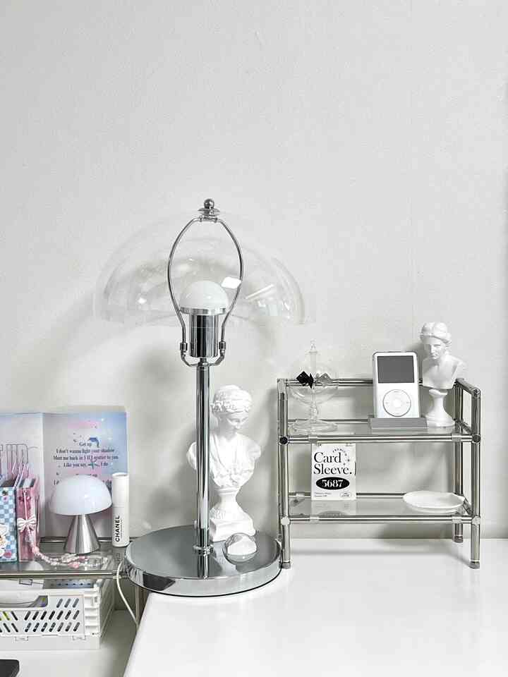 白とシルバーのトーンのデスク、レトロな感覚のアイポッドと彫刻、マッシュルームランプが配置されたミニマルなインテリア空間