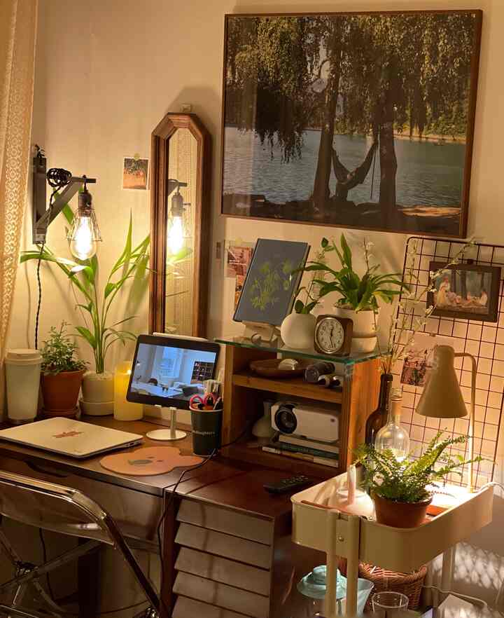 暖かい木目調と植物が調和したアットホームなホームオフィス、壁照明と卓上時計が配置された空間