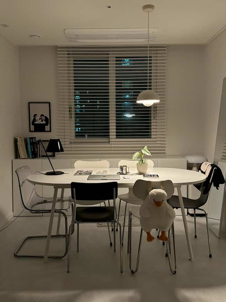 White-toned dining room featuring a central white oval table and assorted chairs in a minimal, modern setting