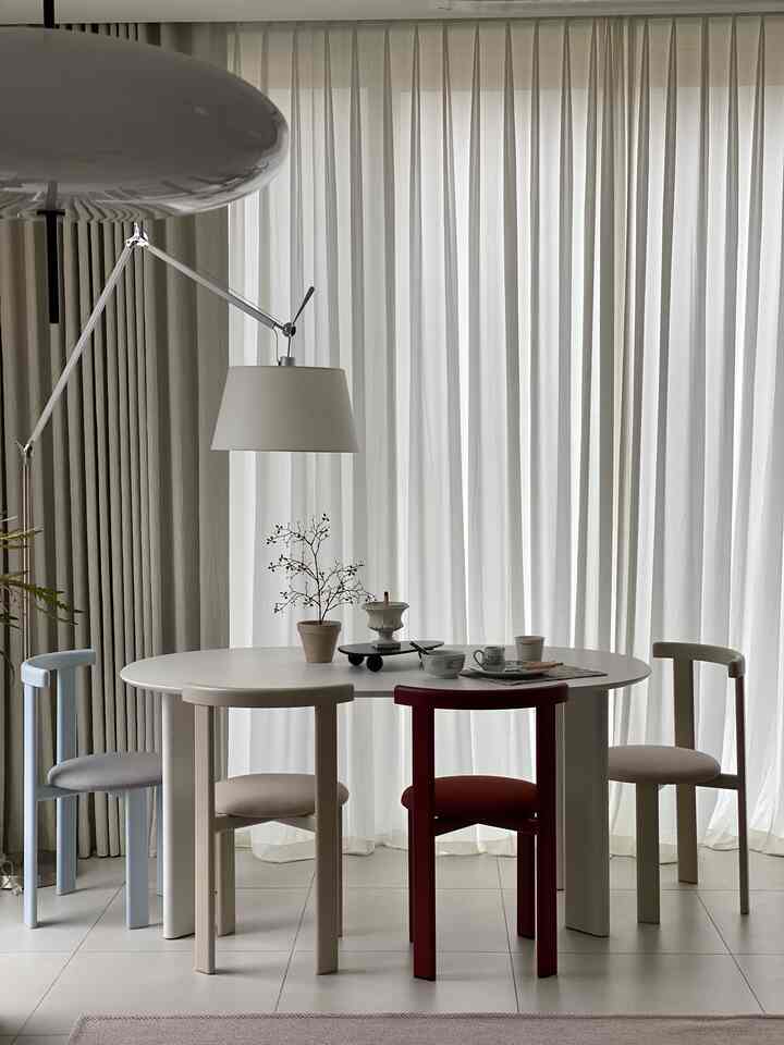 Living room in white and ivory tones featuring a round dining table with colorful dining chairs in a modern interior