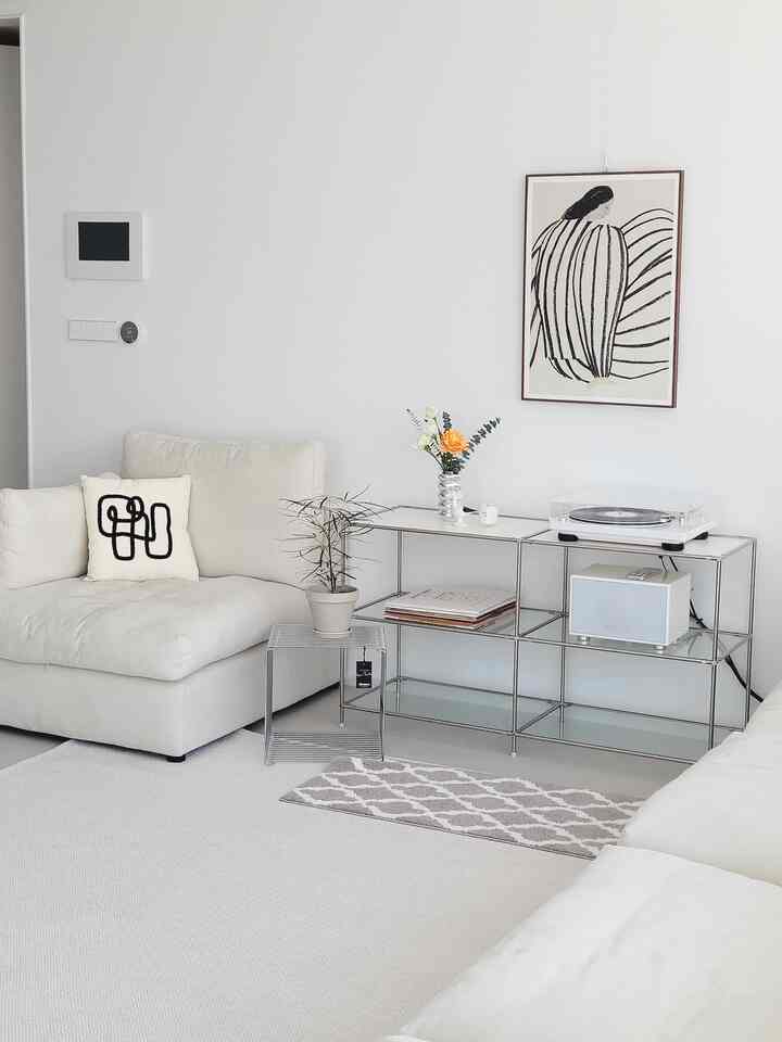 White and silver toned living room featuring simple natural sofas, decorative objets, and plants creating a cozy atmosphere