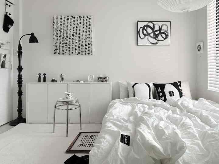 Monotone bedroom featuring white bedding with black accent pillows, minimalist furniture, and modern art for a clean look