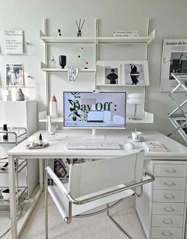 白を基調としたホームオフィス、白いデスクと椅子、壁掛け棚、コンピューターモニターが配置された清潔感のあるインテリア