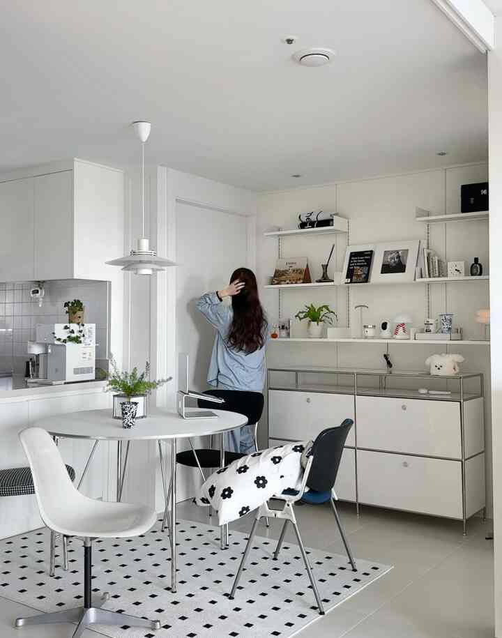 明るいホワイトトーンのモダンダイニングルーム、中央に丸テーブルと椅子が配置され、壁の棚には植物と額縁が飾られたすっきりとした空間