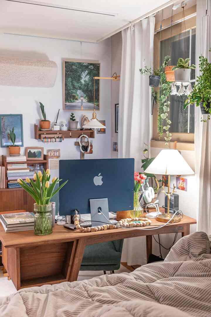 A warm spring mood home office with wood tones and white curtains, featuring a wooden desk holding an iMac and tulip vases