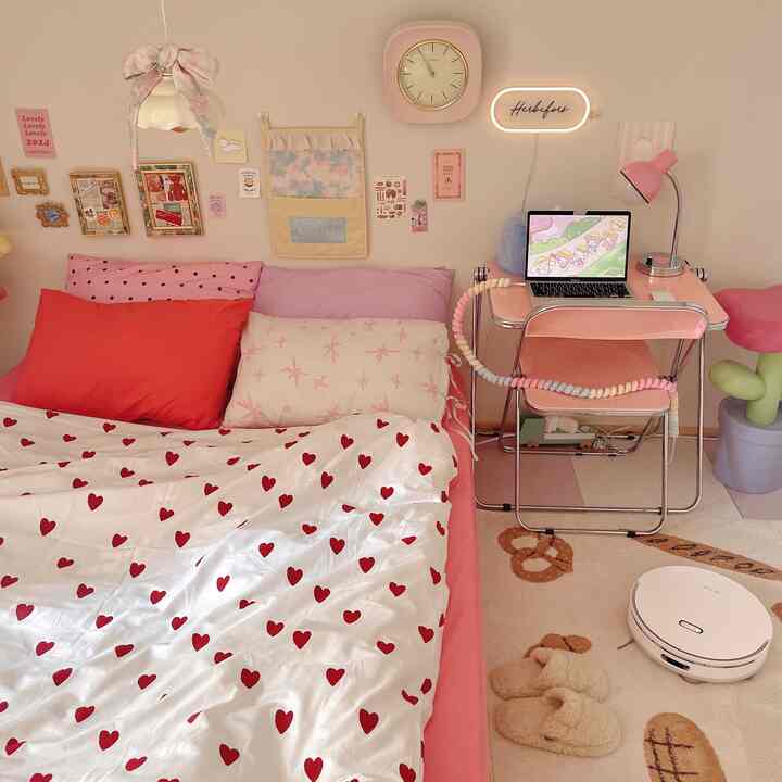 ピンクと白のトーンが特徴のコンパクトな寝室、ハート柄の寝具とデスクが配置された雰囲気のあるホームオフィス空間