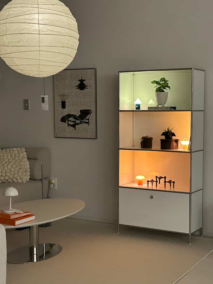 White and beige toned living room featuring modular shelving and sofa table with warm lighting creating a cozy atmosphere