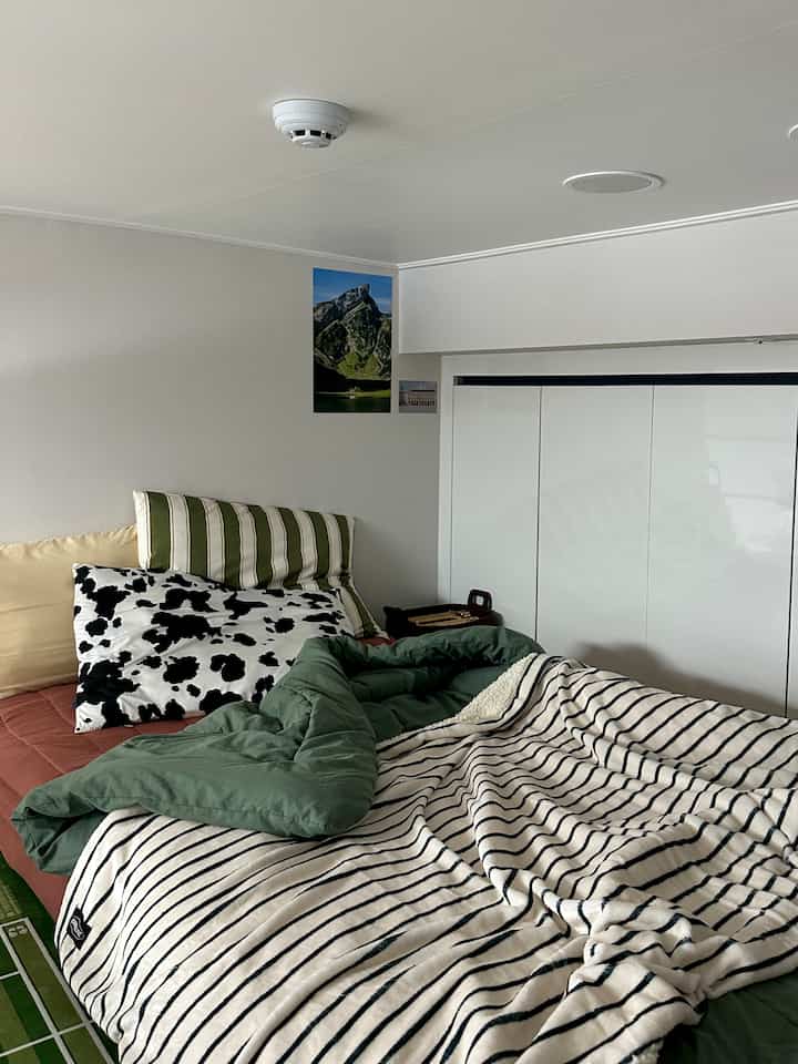 白と緑の色調の寝室、中央にベッドがあり、様々な柄のクッションとブランケットが配置された印象的な空間