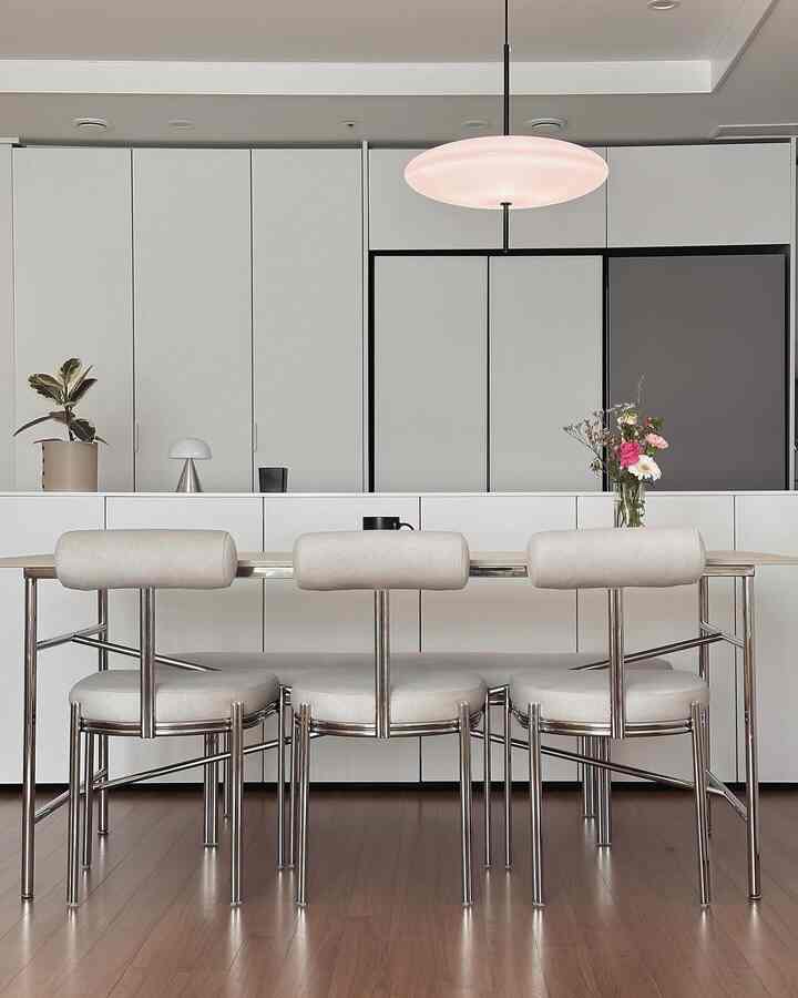Mid-century modern dining room with white walls and wood-tone flooring, featuring chrome metal dining chairs and a pendant light in a simple setting