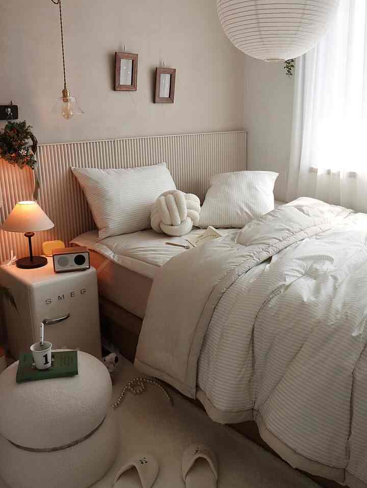 Beige and ivory toned bedroom with striped simple bedding, stool, pendant light, creating a cozy and warm atmosphere