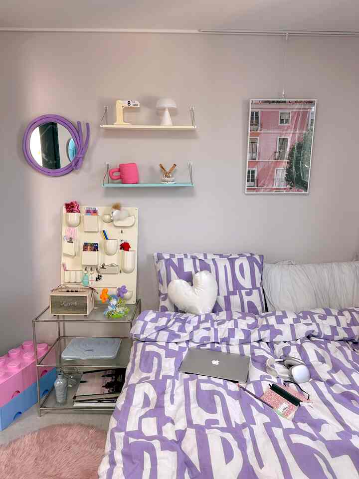 ライトグレーの壁とパープルの寝具が特徴的な寝室。整頓された棚と机があり、モダンでミニマルな雰囲気のインテリア