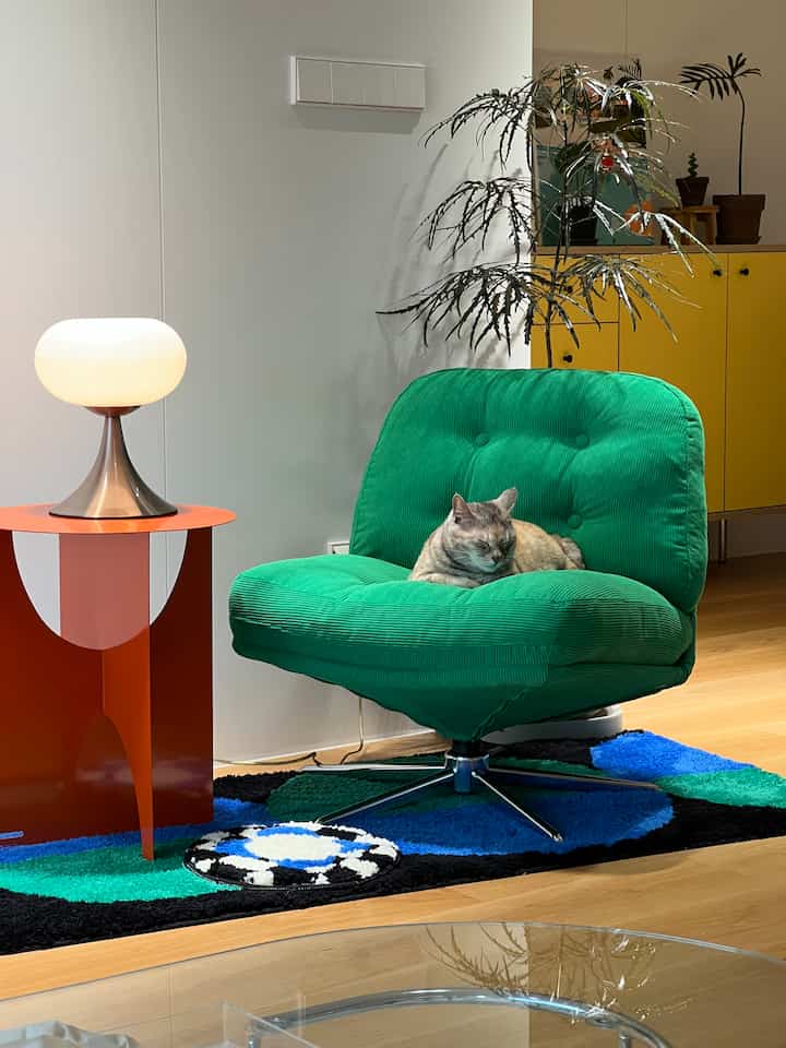 Modern living room featuring a green corduroy armchair, orange side table with lamp, and potted plants creating a cozy vibe