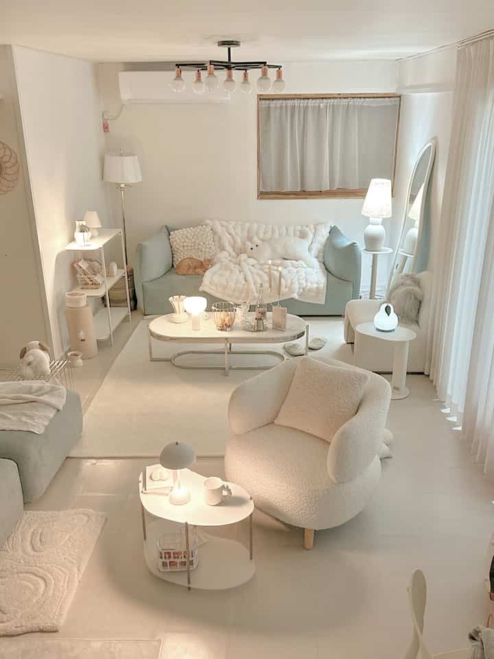 Ivory and white toned living room featuring soft sofas, an armchair, and oval tables with warm lighting creating a cozy atmosphere