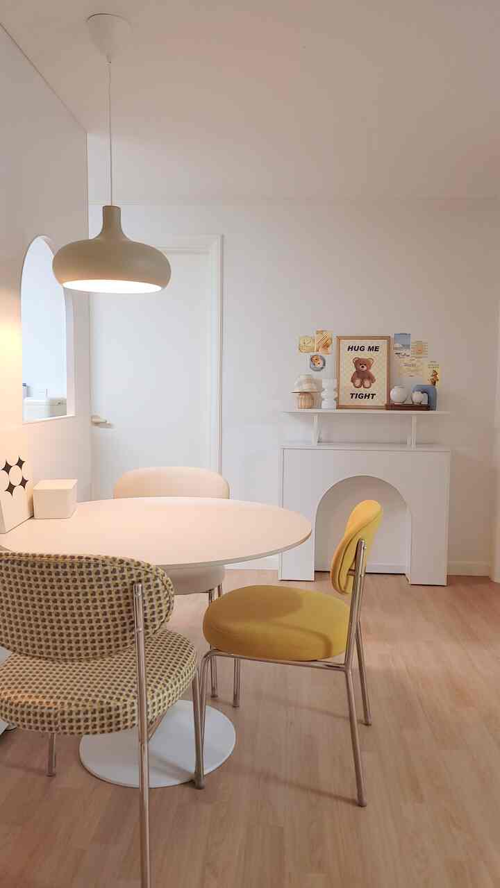 A white and yellow toned dining room featuring a dining table, chairs, fireplace-style console, and posters creating a cozy cafe atmosphere