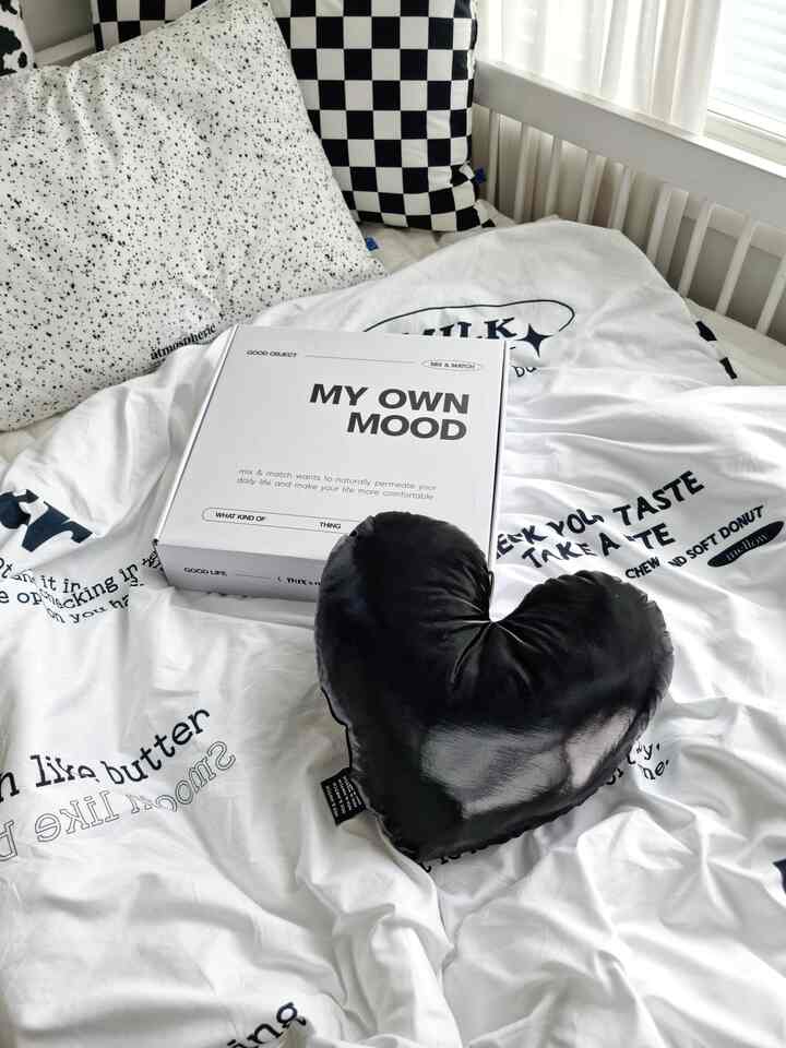 White and black toned kids' bedroom featuring a heart-shaped cushion and casual bedding in a simple setting