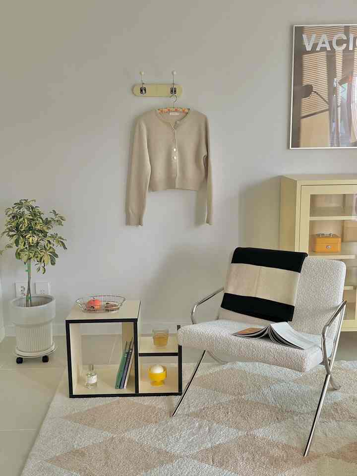 A cozy living room in white and beige tones featuring a lounge chair, throw blanket, and tidy storage cabinet