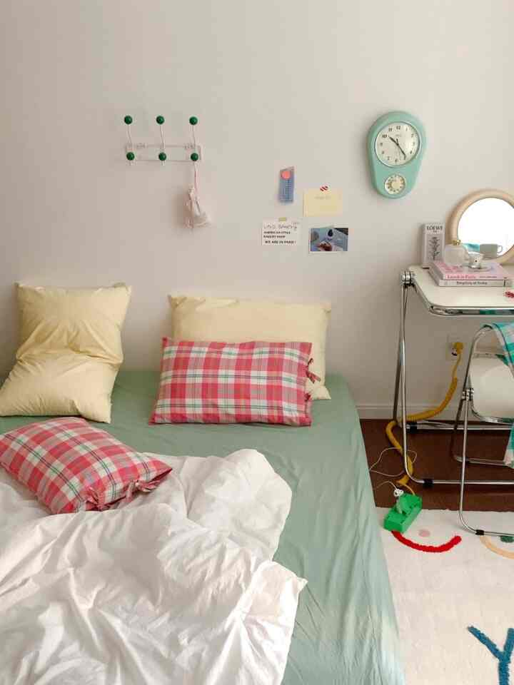 Bedroom with white walls and green bed sheets, yellow and pink checkered pillows, featuring a clean and cozy atmosphere