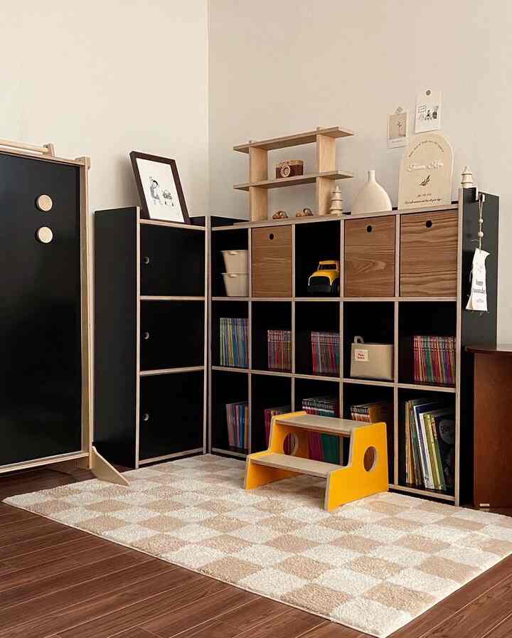 Natural wood tone and black kids' room featuring a bookshelf, yellow kids' step stool, and a checkered rug in a tidy space