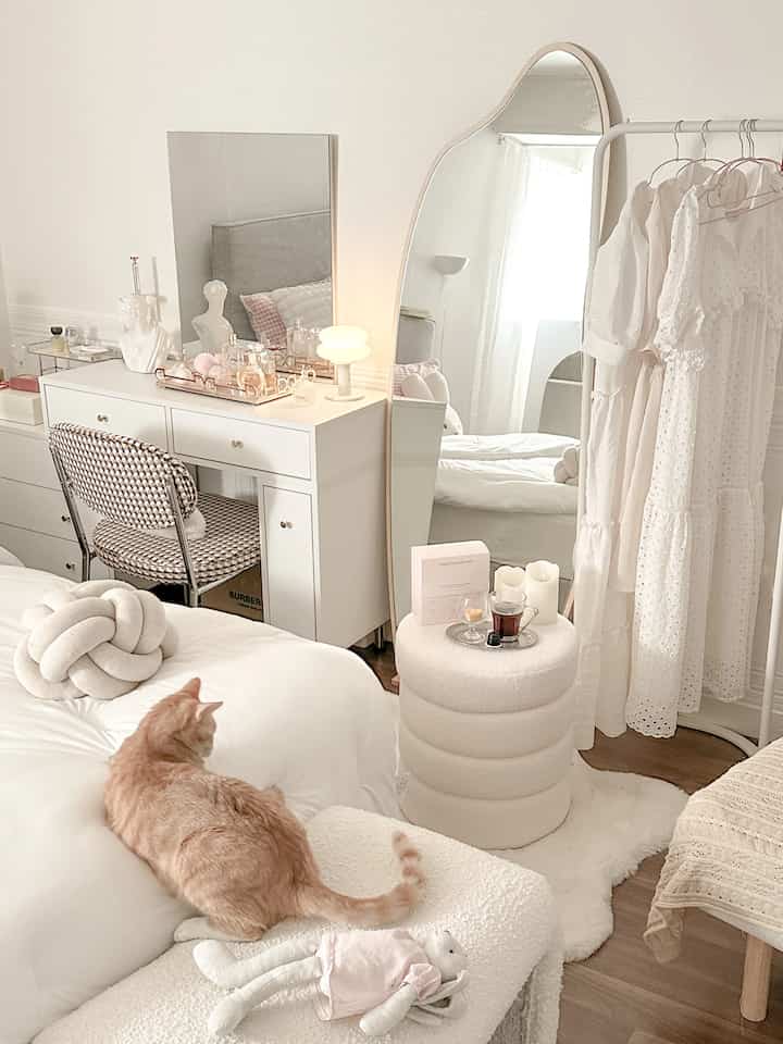 A white and natural toned bedroom featuring a vanity, round stool, and clothes rack in a warm and cozy atmosphere