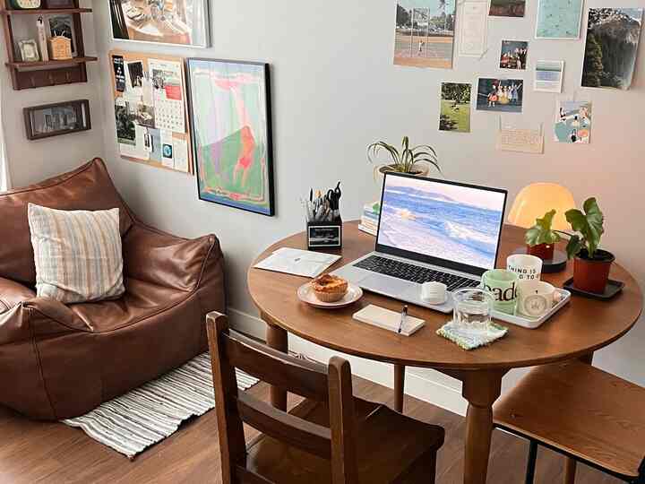 ブラウンレザーソファと木製の丸テーブル、ポスターや写真が壁に貼られたナチュラルモダンスタイルのコンパクトなリビングルーム