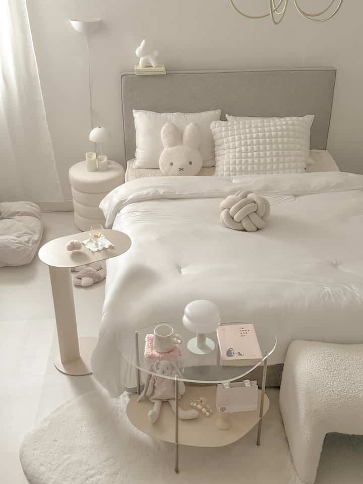 Ivory and beige toned bedroom featuring large central bed, various cushions, side tables with table lamps and decor creating a cozy atmosphere