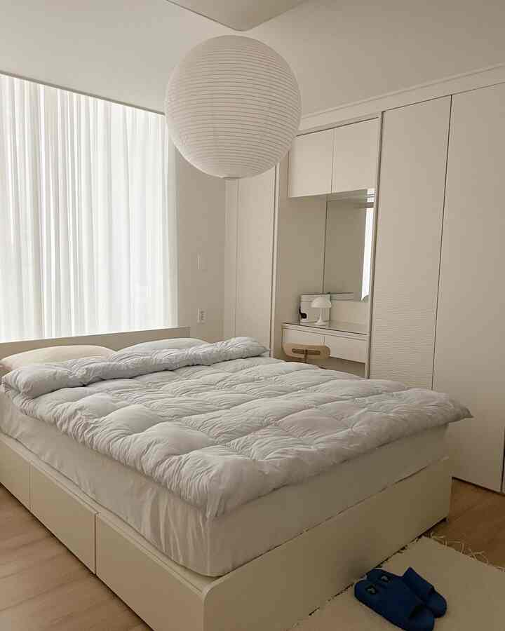 A bedroom dominated by white and natural tones featuring a large bed and integrated storage in a simple setting