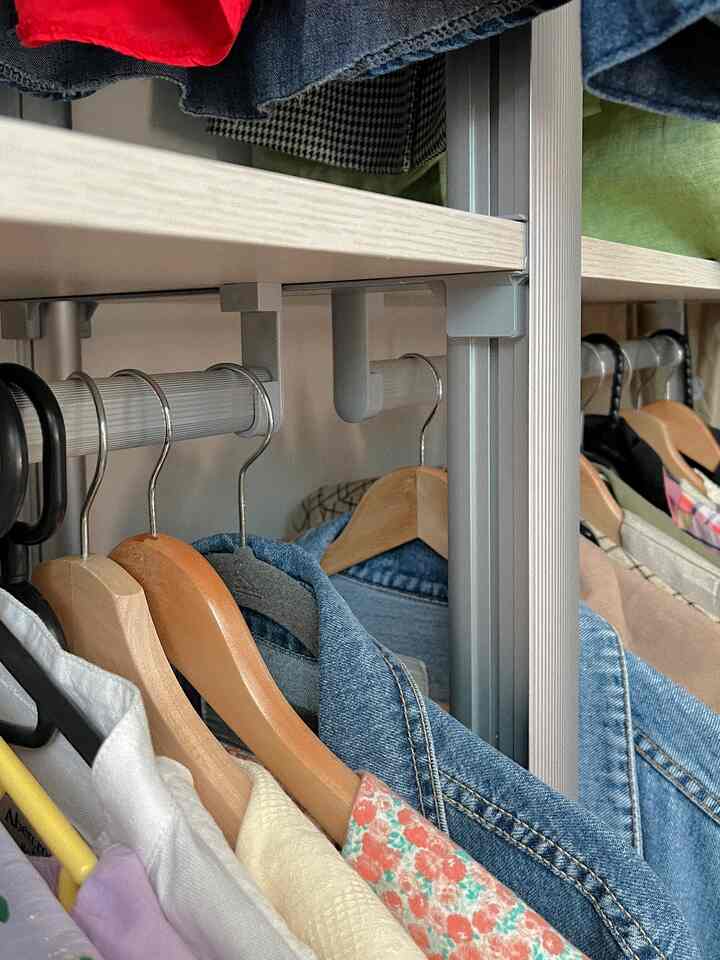 木目調とホワイトが調和したウォークインクローゼットのシステムハンガー、さまざまな服と木製ハンガーが整然と配置された印象的な空間