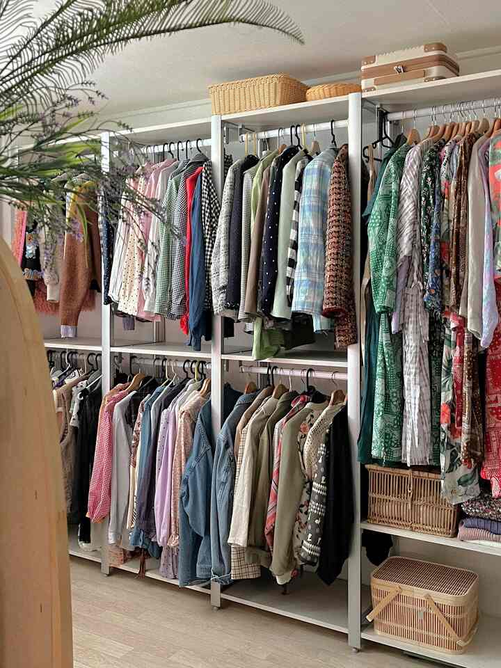 白いフレームのシステムハンガーと木目調の床が調和した清潔感のあるウォークインクローゼット