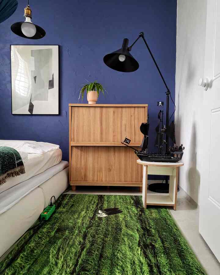 Modern boys' bedroom with dominant navy blue wall, wood furniture, and green rug creating a calming atmosphere