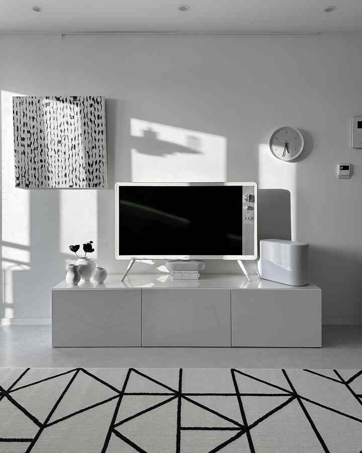 A simple white and black living room featuring a central white TV stand and geometric rug with a clean atmosphere