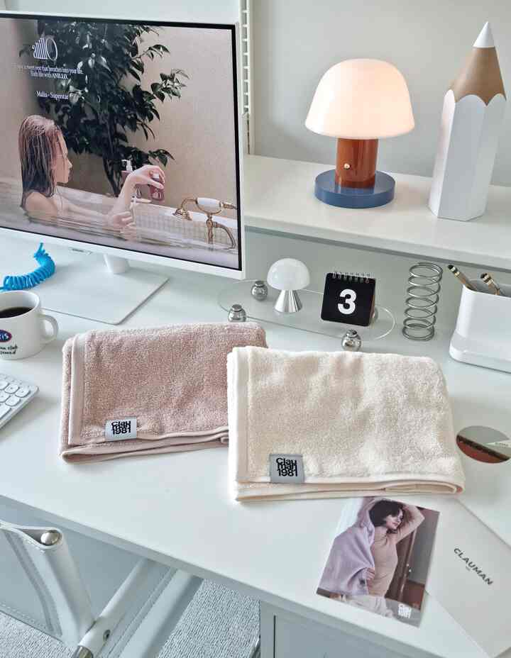白を基調としたホームオフィス空間、白いデスクの上にブリッシュピンクとアイボリーのタオル、デスクライトが配された清潔感のあるインテリア