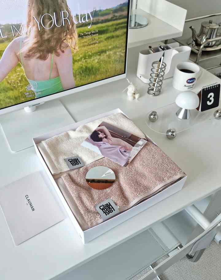 白いトーンのホームオフィスデスクに高級タオルセットとモダンなデスク用品が整頓された清潔感のある空間