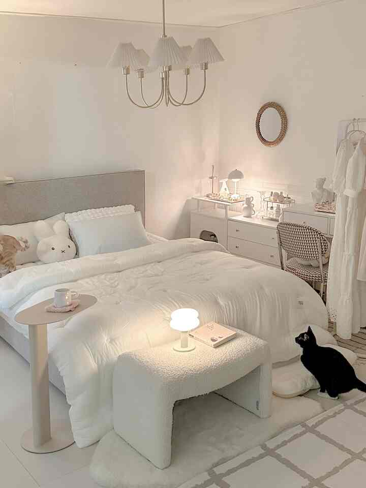 明るい白色調の寝室、中央に大きなベッドと柔らかいモーダル寝具があり、右側に居心地の良い化粧台と照明が配置された雰囲気のあるインテリア