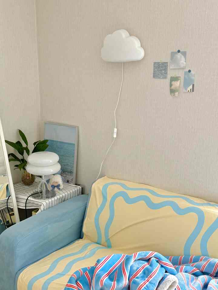 パステルイエローとブルーのトーンの子供部屋、ソファと雲型の壁照明、感性豊かな写真が配置された温かみのある空間