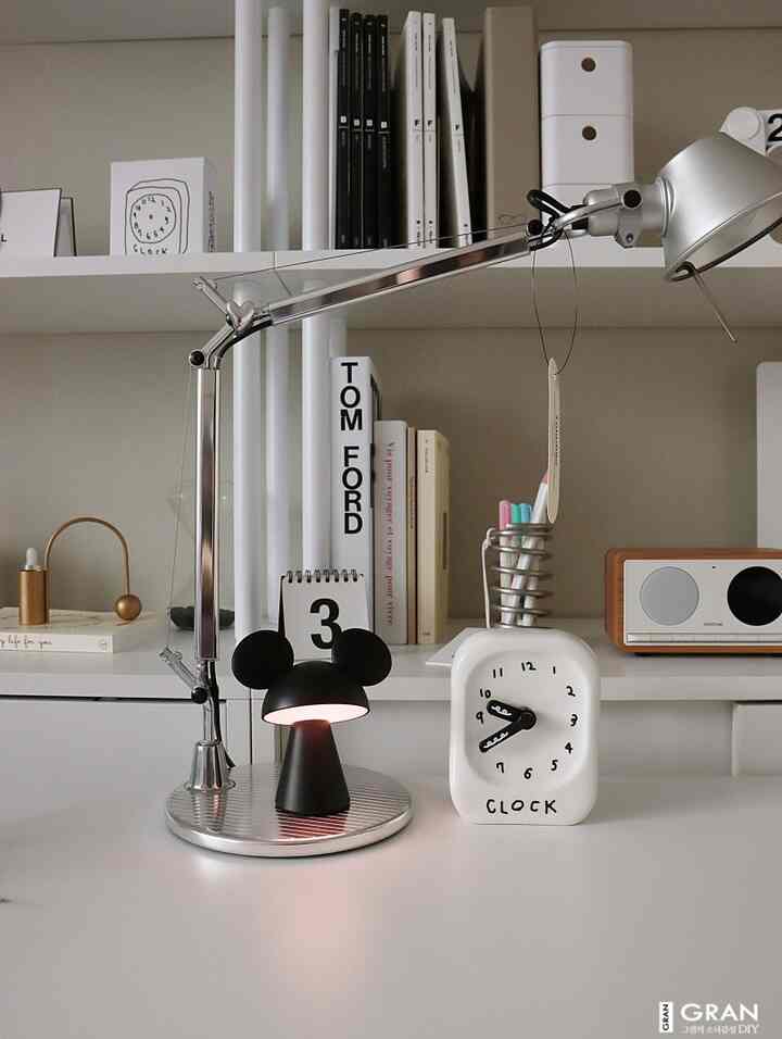 White-toned desk and shelving space featuring a Mickey table lamp and unique clocks, creating a cozy home office atmosphere