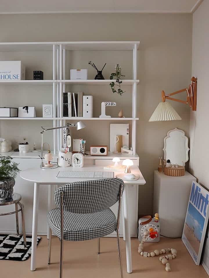 Beige walls and white furniture define a single-person home office study featuring desk lamps, clock, and accessories in a clean, natural setting