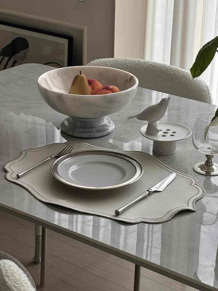 Natural modern dining room in white and gray tones featuring marble table, silver cutlery, and a marble bowl with decorative fruit