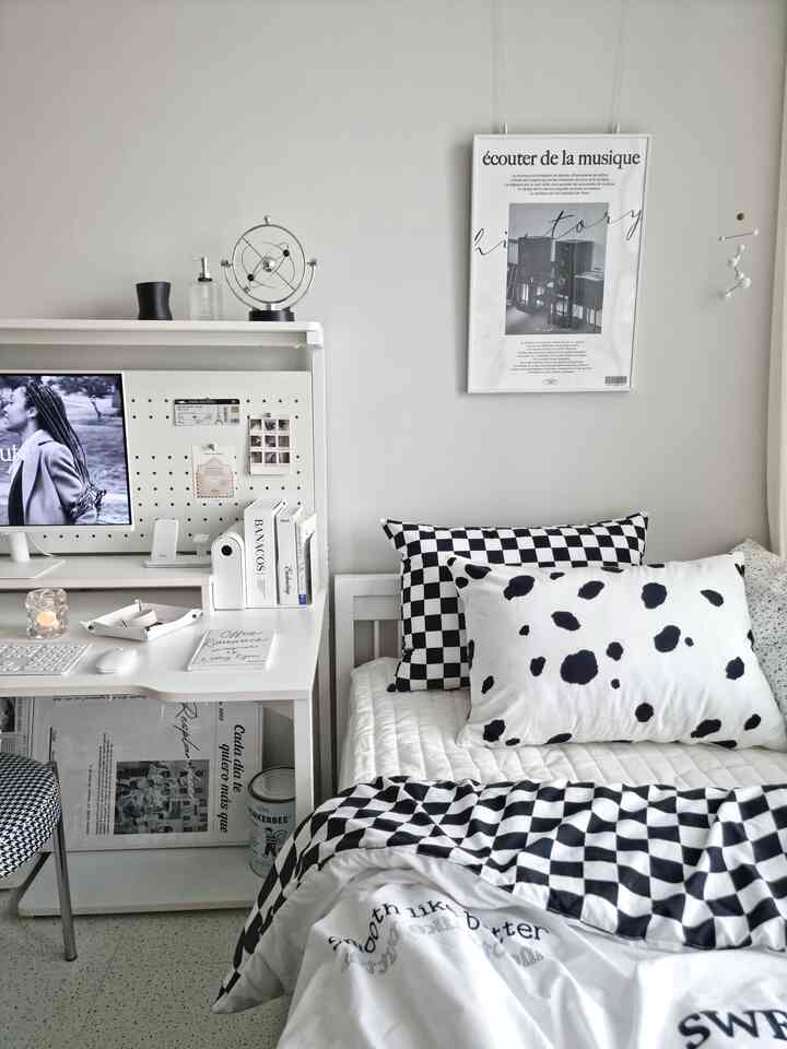 A white and black toned kids' room featuring a minimal desk, bed with checkered bedding, and a modern-style poster