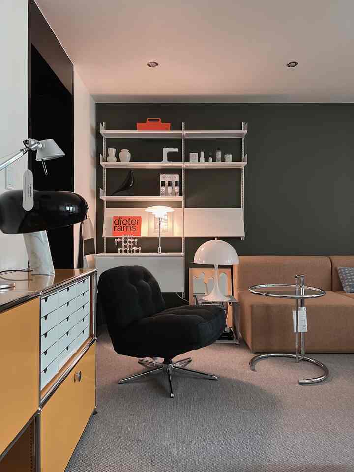Living room with natural tones and dark green wall, featuring a black armchair, beige sofa, modern table lamps, and a chrome side table.